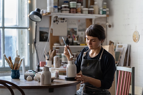 Female craft crockery and potter tableware master at workplace wearing apron closeup